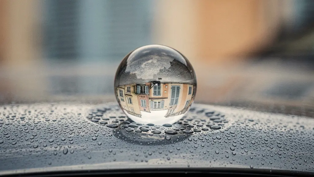 Gros plan sur une boule de verre réfractant la lumière posée sur un capot de voiture, métaphore de l'effet multiplicatif du coefficient bonus-malus